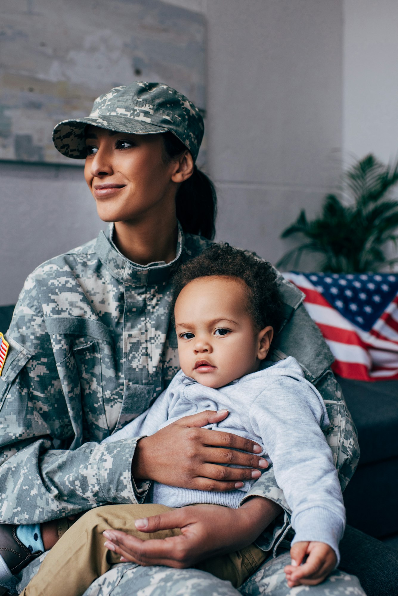 african american female soldier in military uniform with baby boy at home, with american flag on